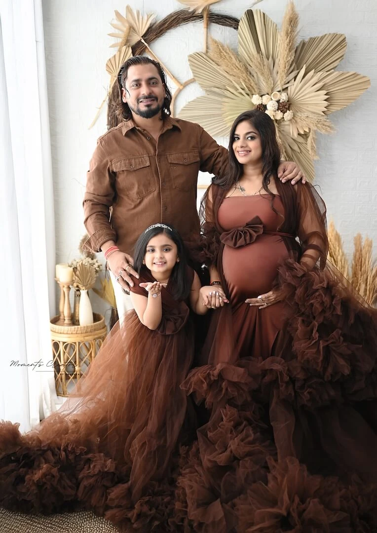Family maternity photoshoot in a brown ruffled gown with husband and daughter at a Delhi studio